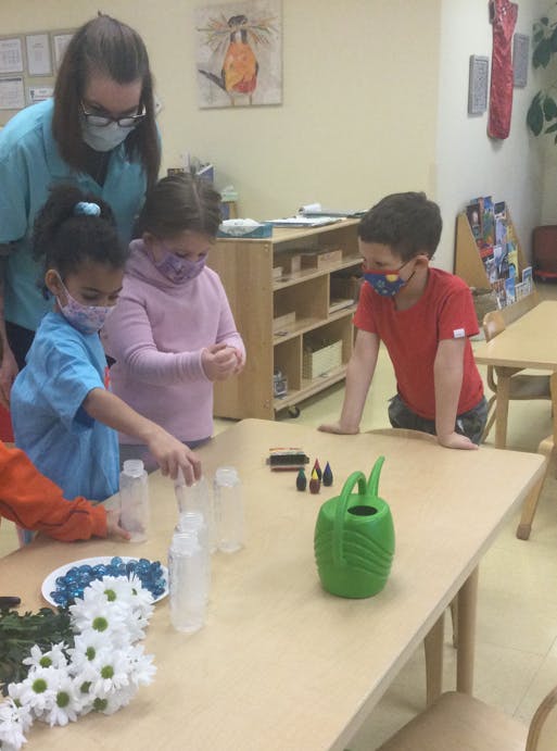 Adult and children in masks at a table with bottles and craft supplies