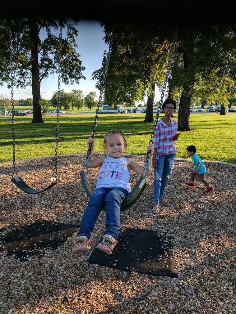 Child on a swing with a person and another child in the background
