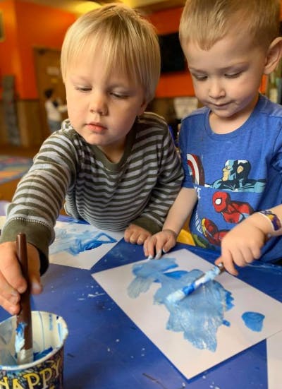 Two children painting with blue paint on paper