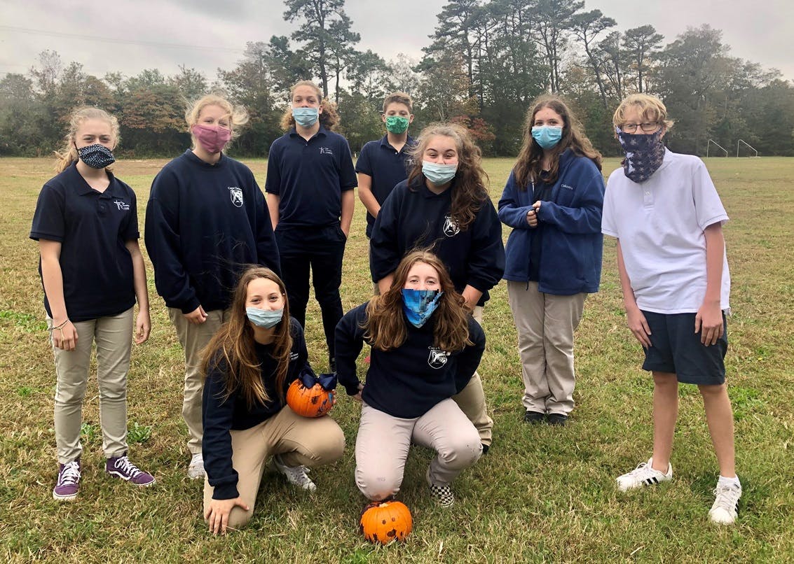 Group of teens and children wearing masks and holding pumpkins in a field