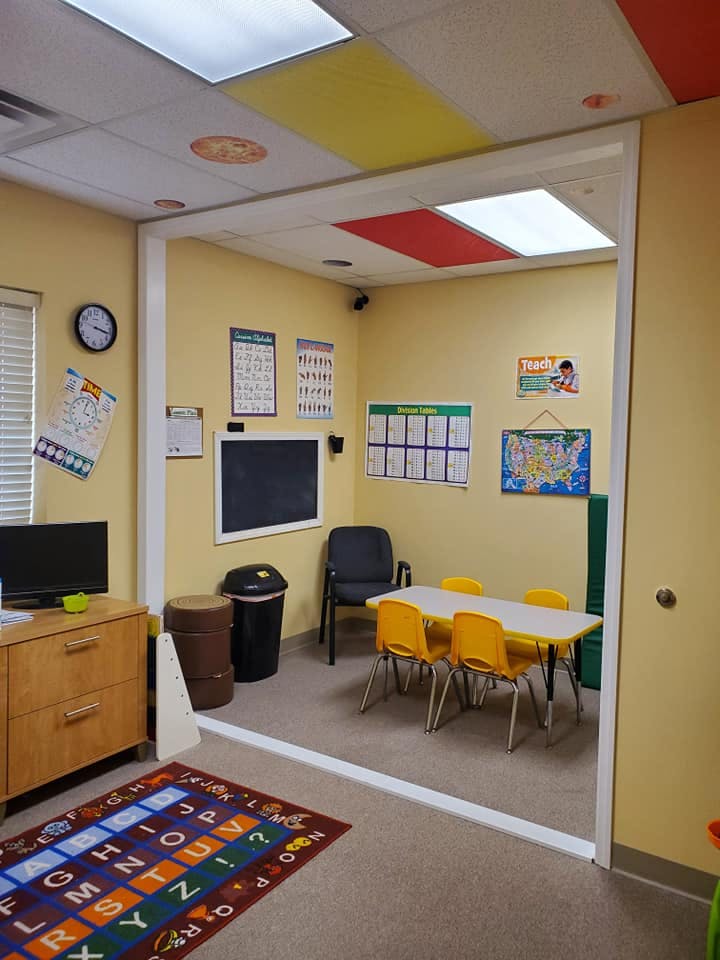 Classroom with small table and chairs, chalkboard, and alphabet rug