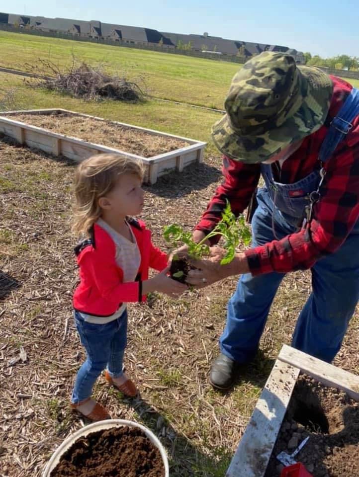Person in camouflage hat handing a plant to a child