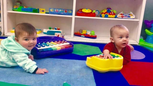 Two babies playing with toys on a colorful mat