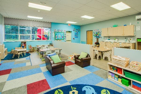 Classroom with small tables and chairs, armchairs, and a colorful rug