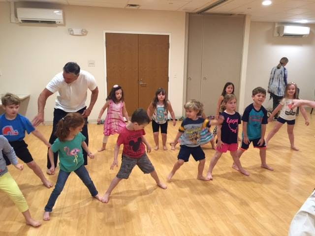 Adult and children in a room with wooden floors, all in a wide stance