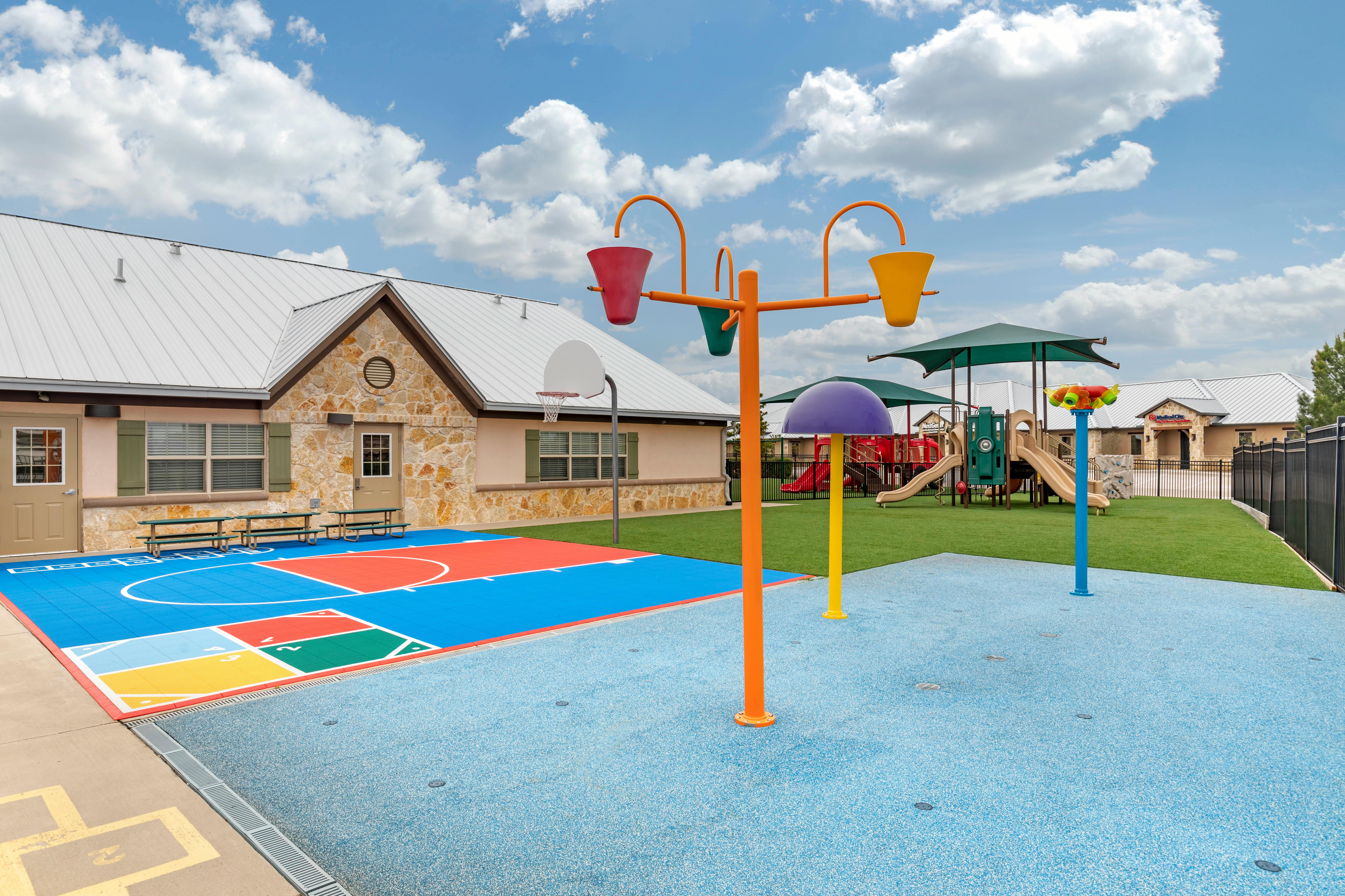 Colorful outdoor play area with a basketball court, splash pad, and playground