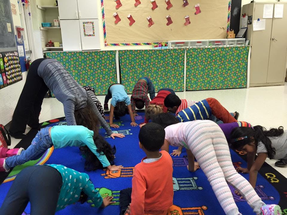 Adult and children doing yoga poses in a classroom