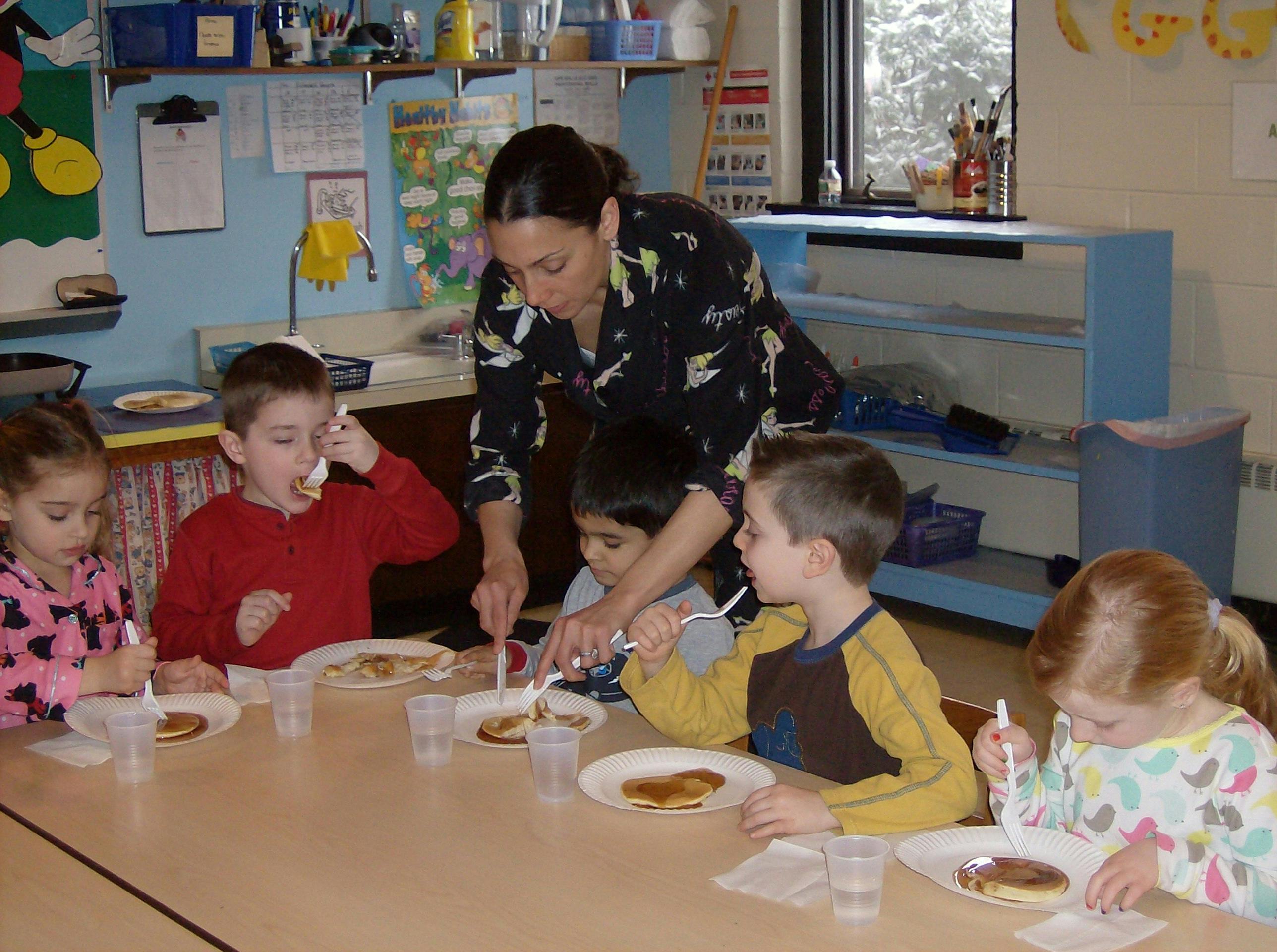 Adult helping children eat pancakes at a table