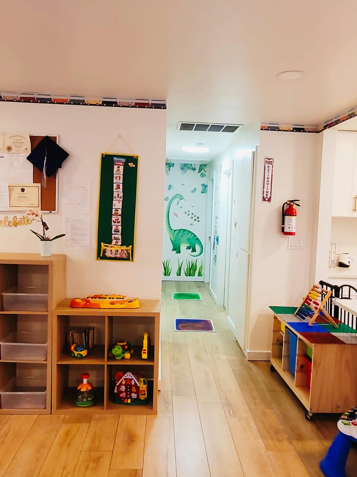 Childcare room with wooden shelves containing toys and dinosaur wall art