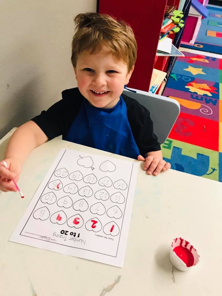 Child tracing numbers on a worksheet with a red marker