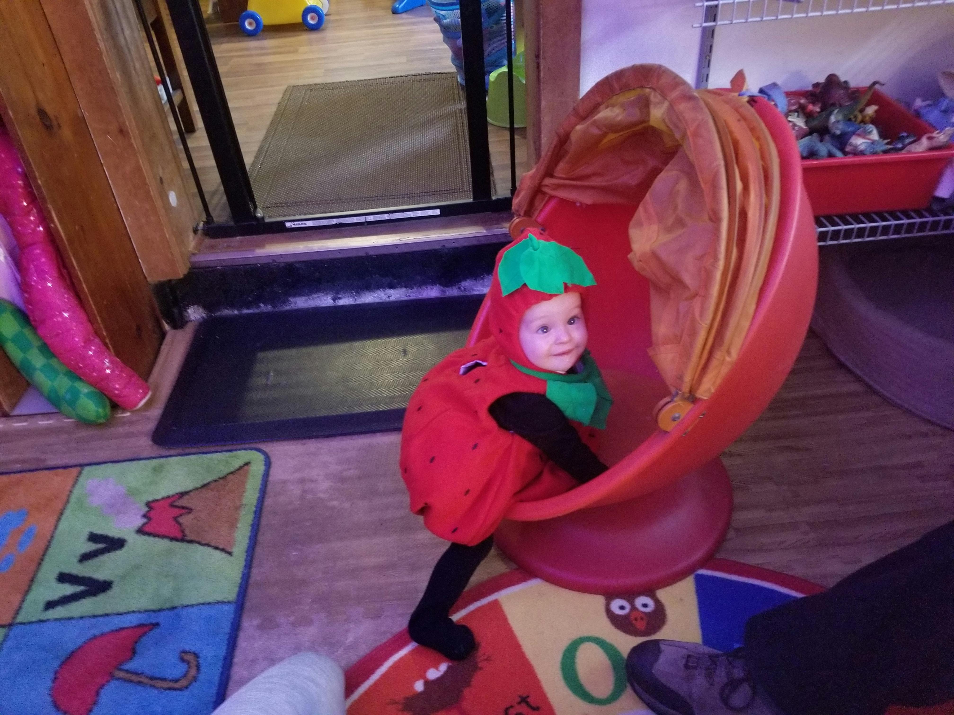 Child in a strawberry costume sitting in a red chair