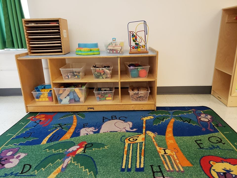 Classroom with a wooden shelf unit holding clear bins of supplies and a colorful rug
