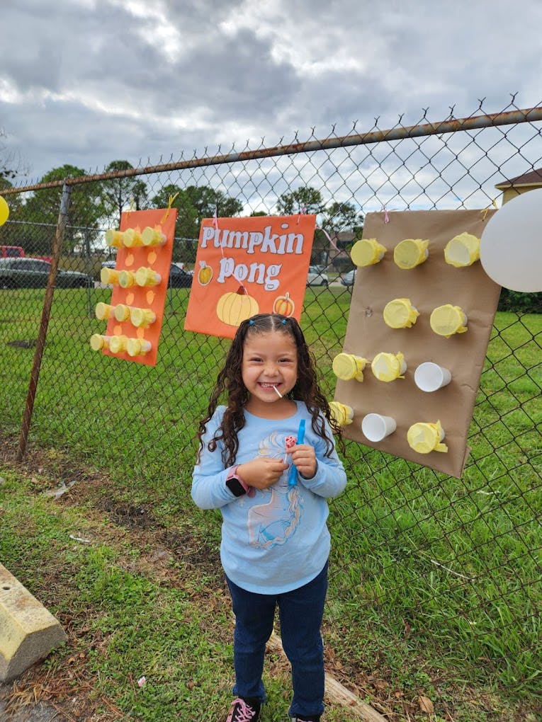 Child holding a lollipop next to a Pumpkin Pong game