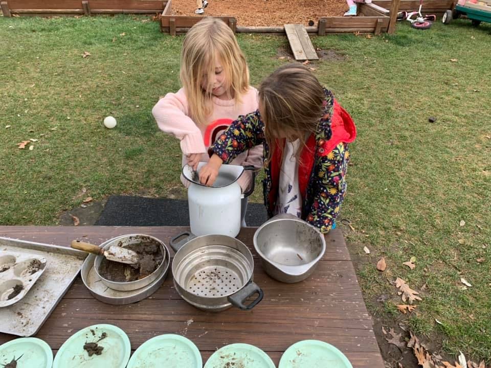 Two children playing with mud and kitchen utensils outdoors