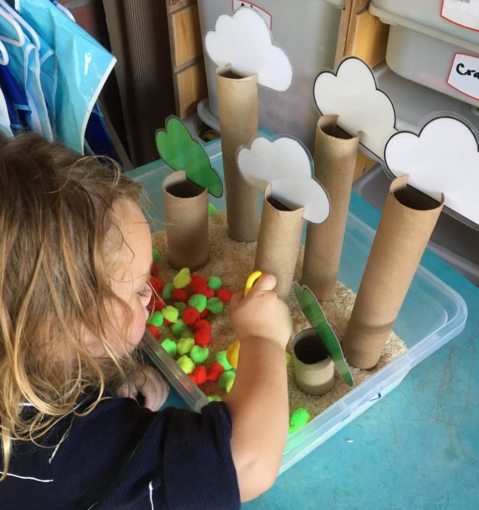 Child playing with a sensory bin with cardboard tubes and pom-poms