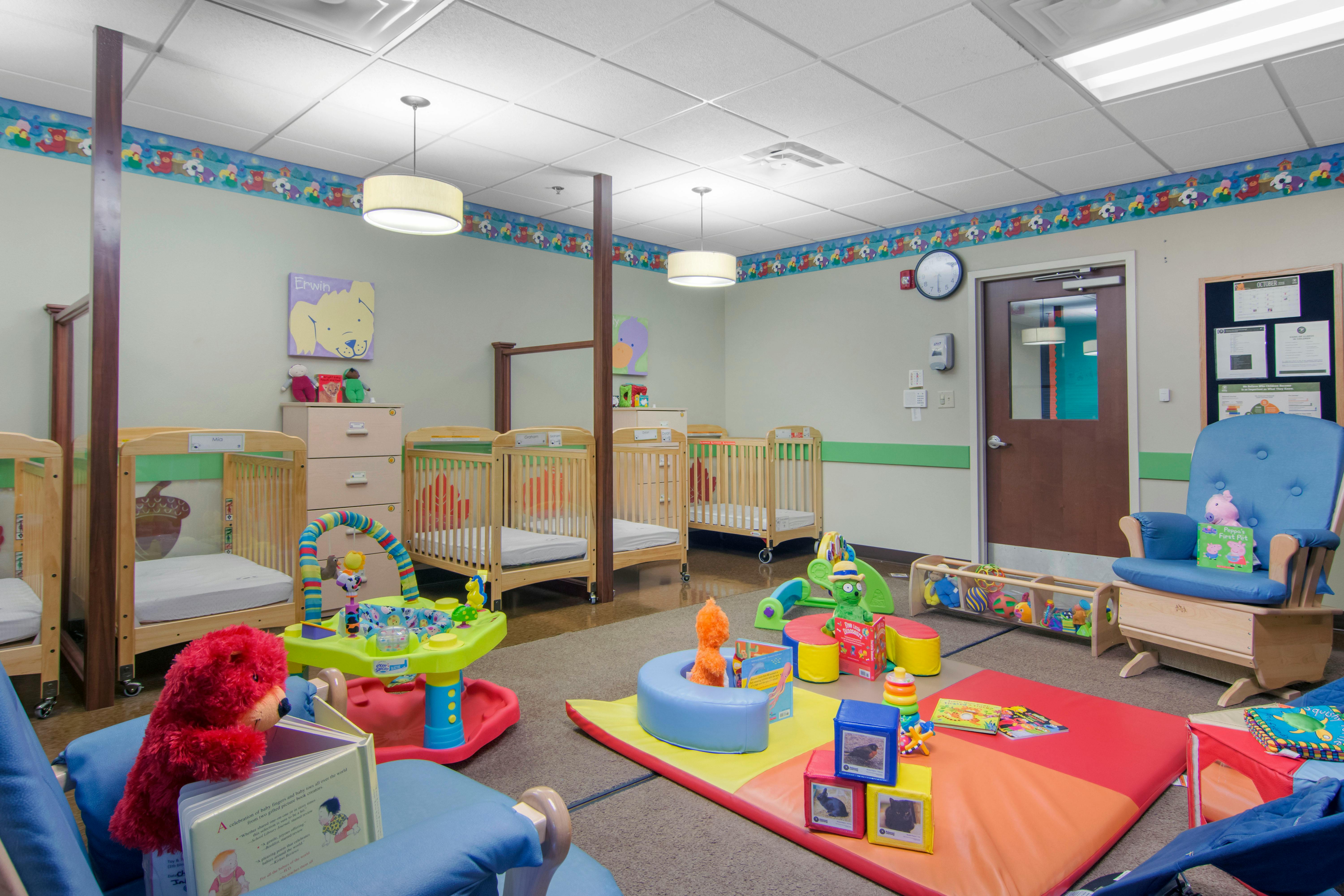 A brightly lit nursery room with several wooden cribs and various colorful toys