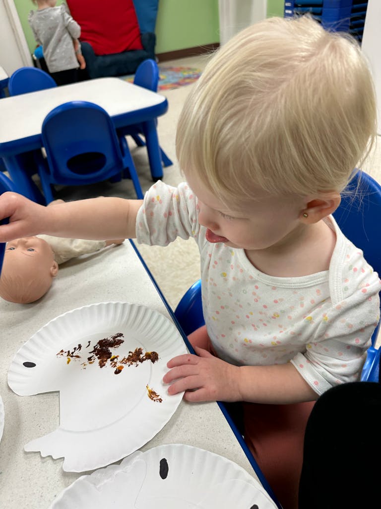 Child in a high chair playing with a doll head and a paper plate