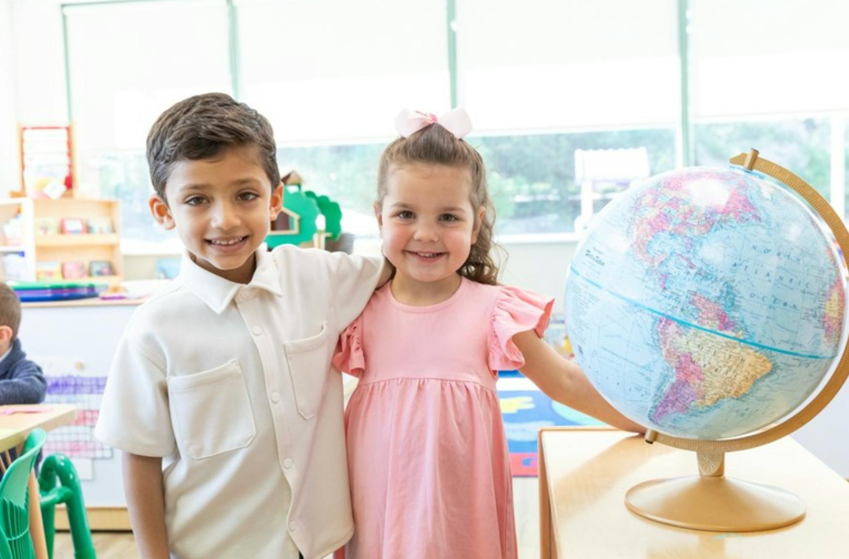 Two children standing next to a globe in a classroom