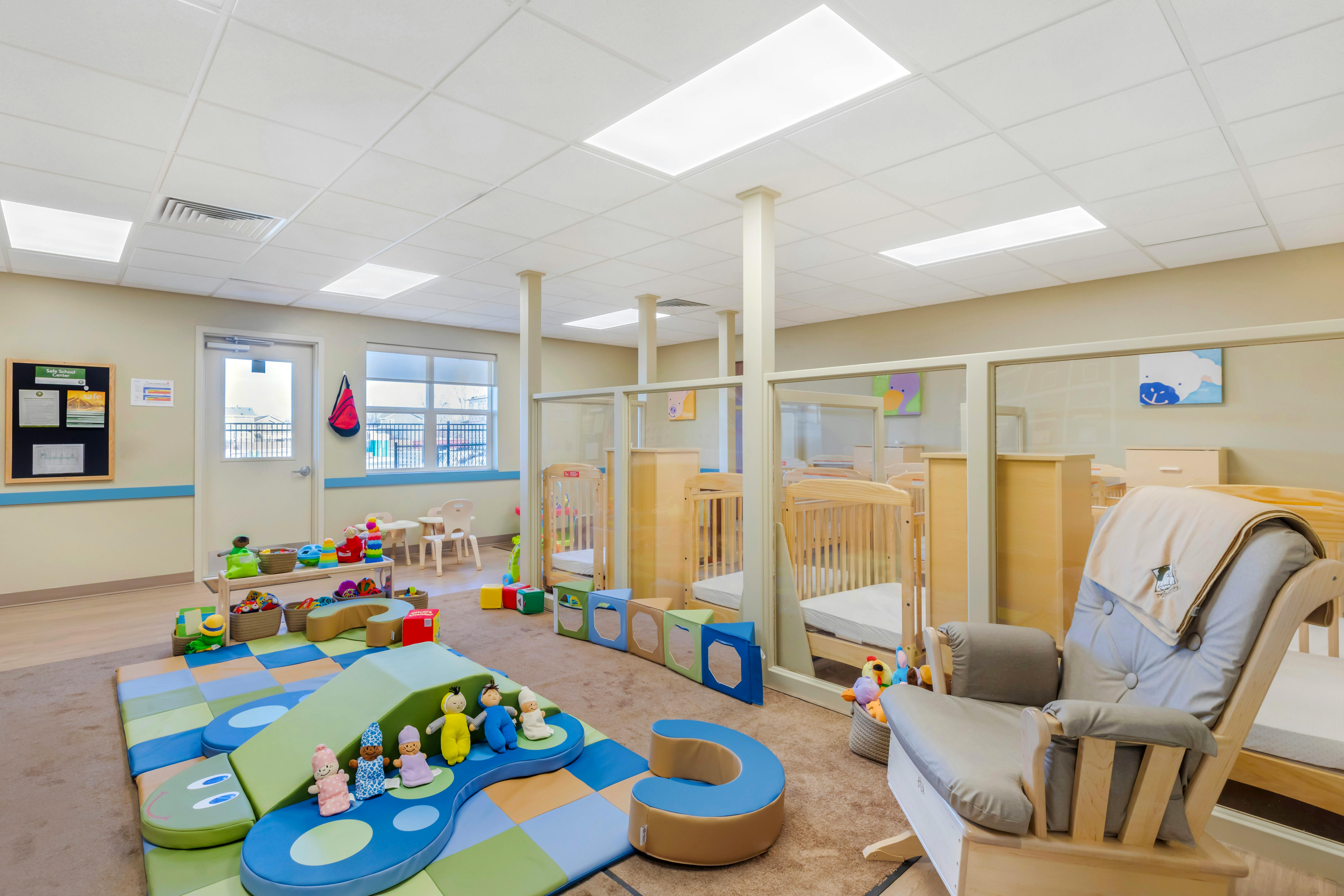 Daycare room with play mat, toys, cribs, and a rocking chair