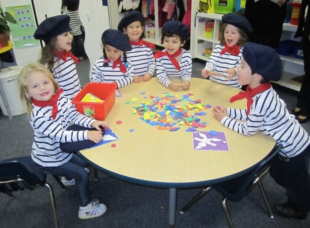 Children in striped shirts and berets around a table with colorful shapes