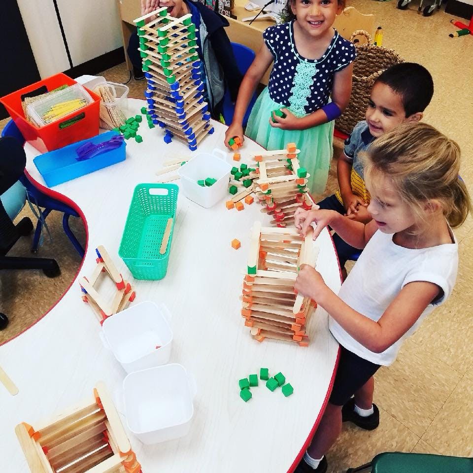 Three children building structures with craft sticks and small blocks