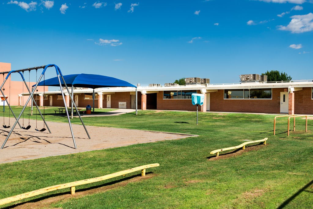 School playground with swings, a blue shade structure, and a building