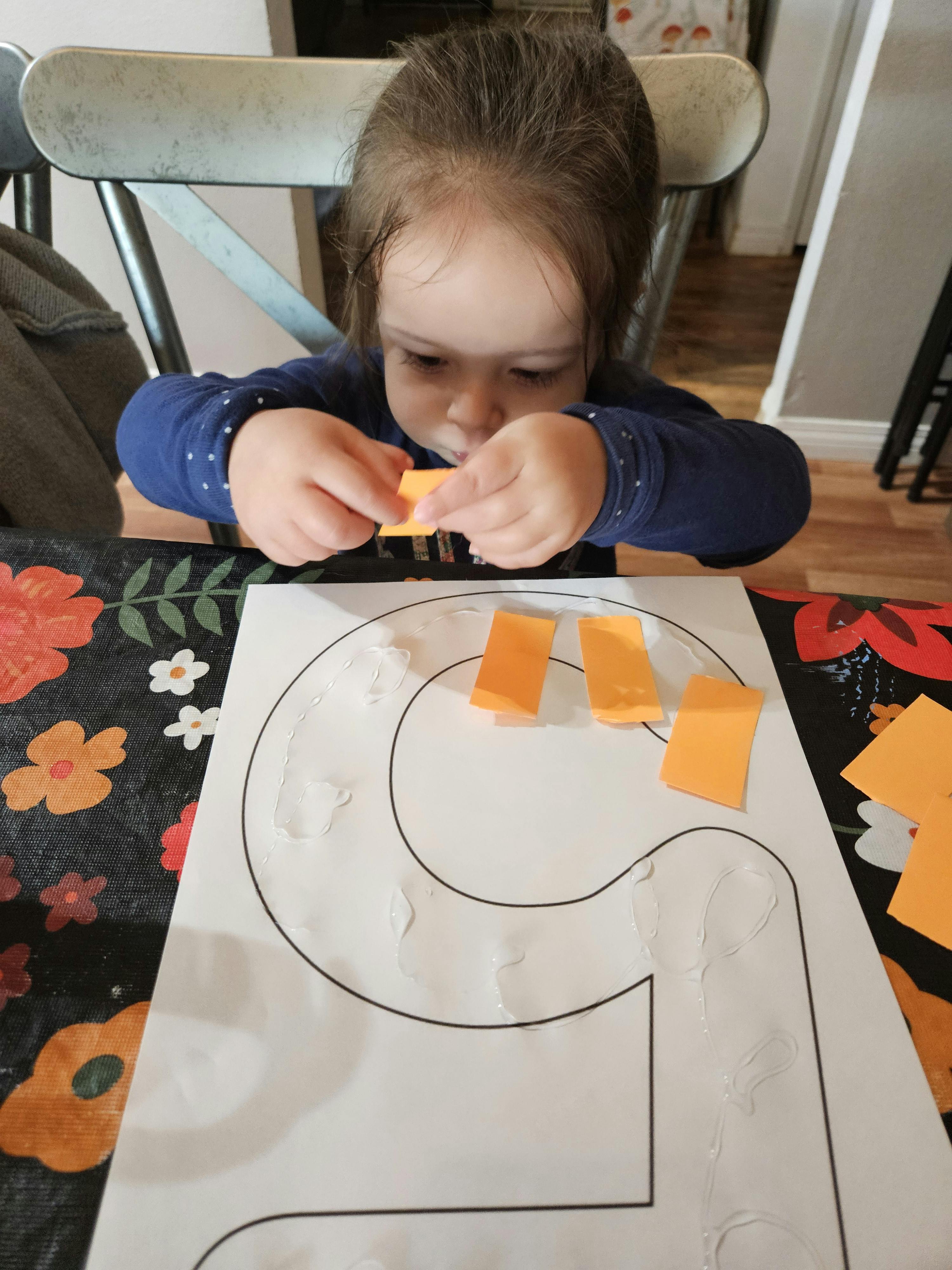 Child gluing small paper shapes onto a paper outline of the number five