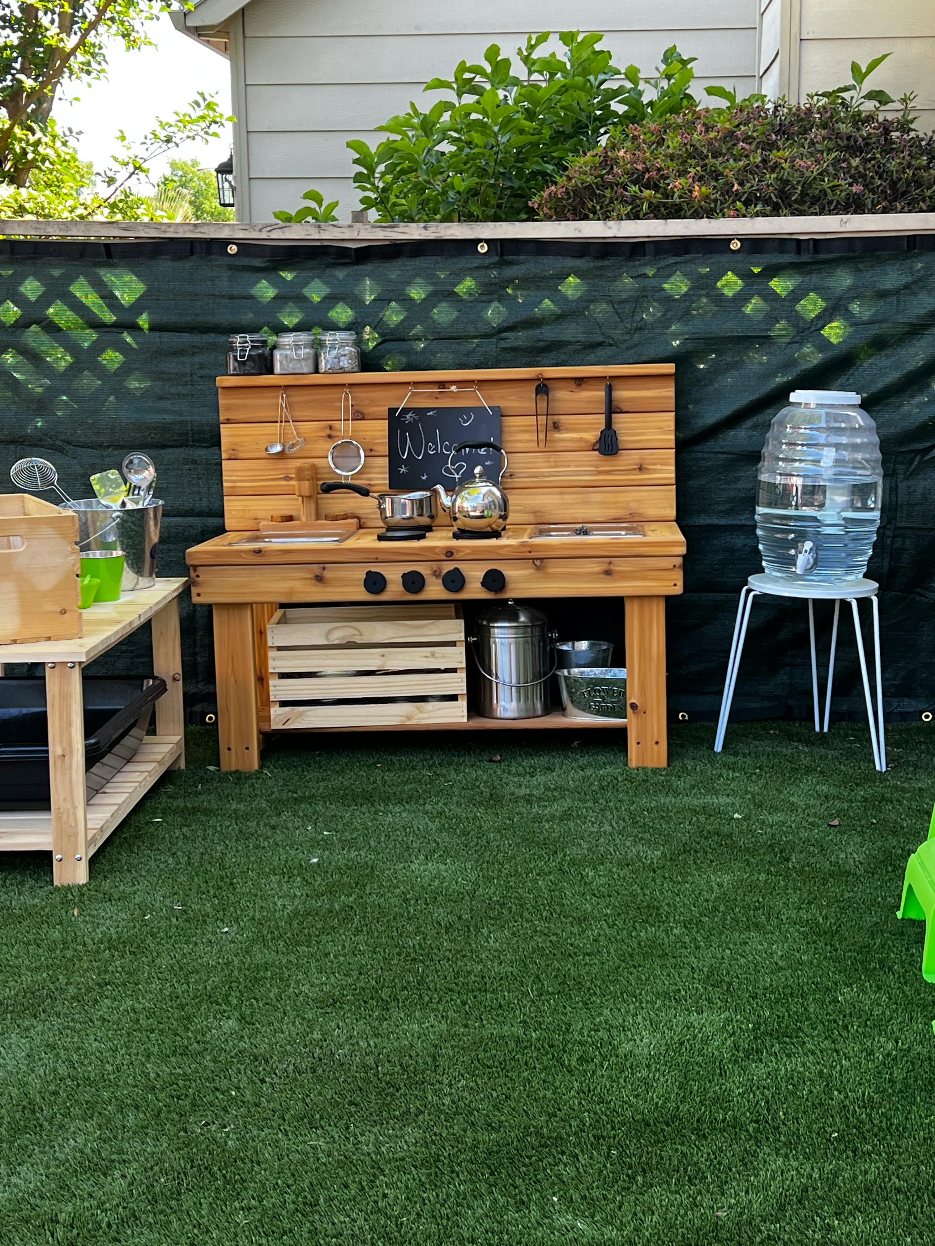 Outdoor wooden play kitchen with pots, pans, and a water dispenser