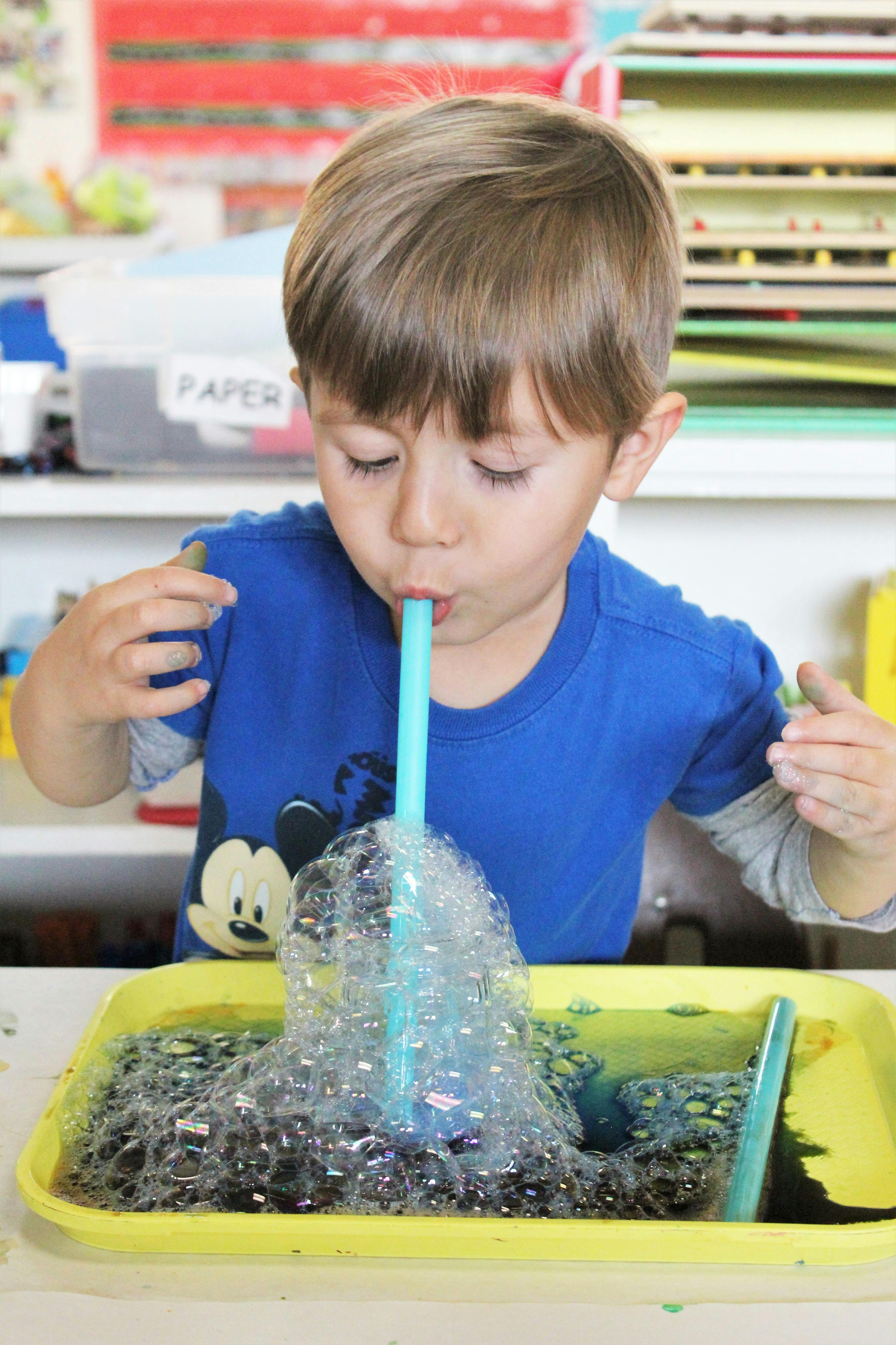 Child blowing bubbles with a straw into a tray of liquid