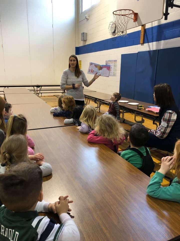 Person reading a book to a group of children in a large room
