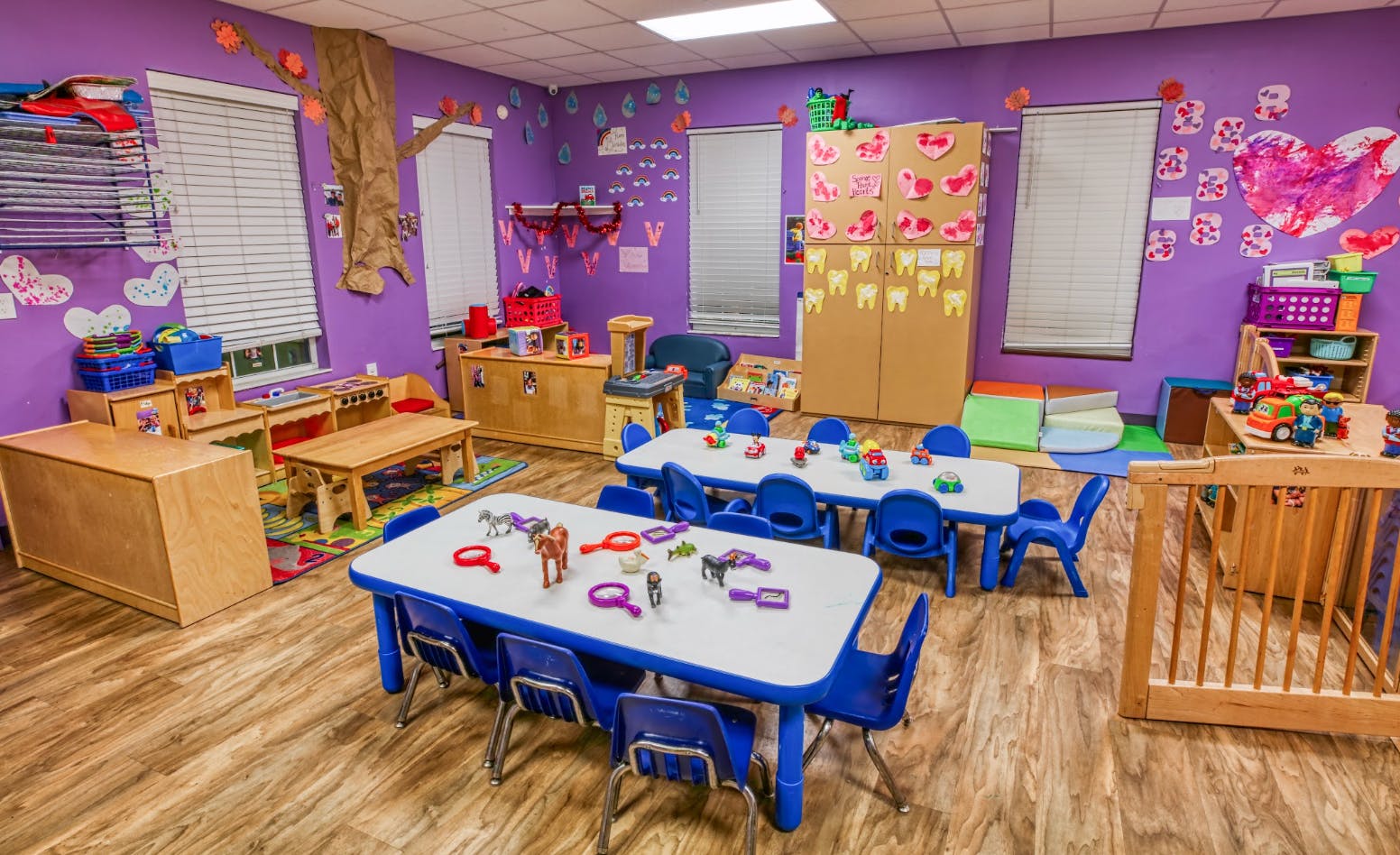 A classroom with small tables and chairs, toys, and purple walls with decorations