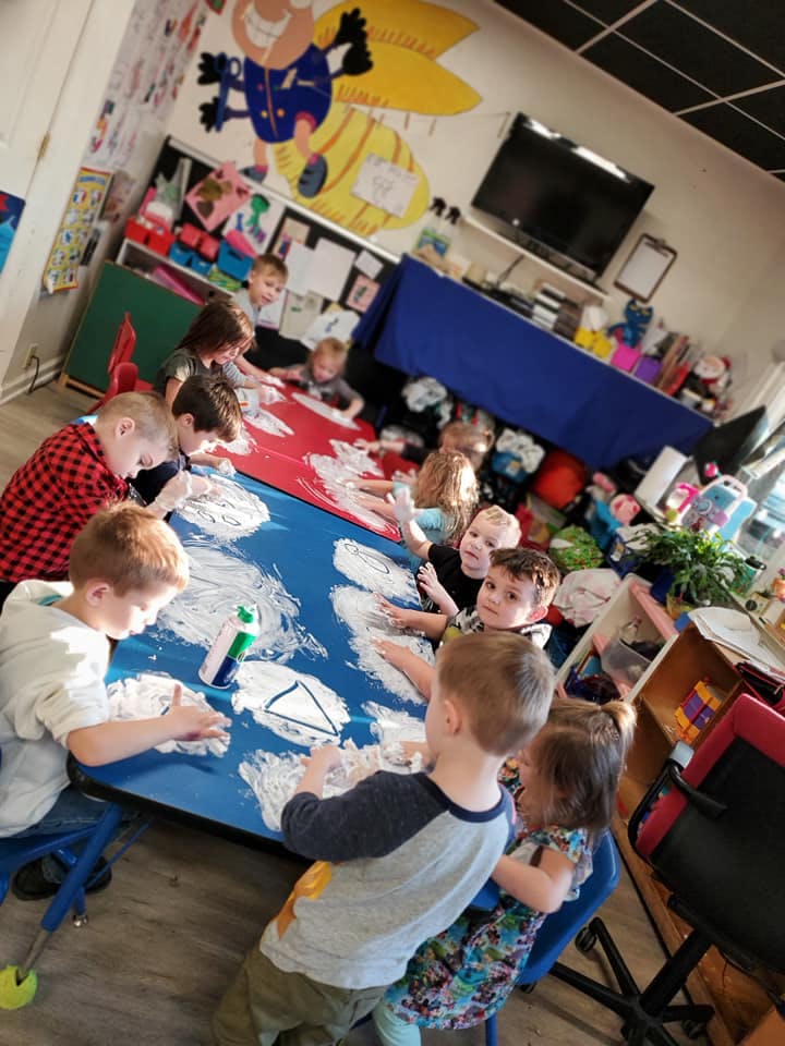 Children gathered around a table doing an art activity with white paint