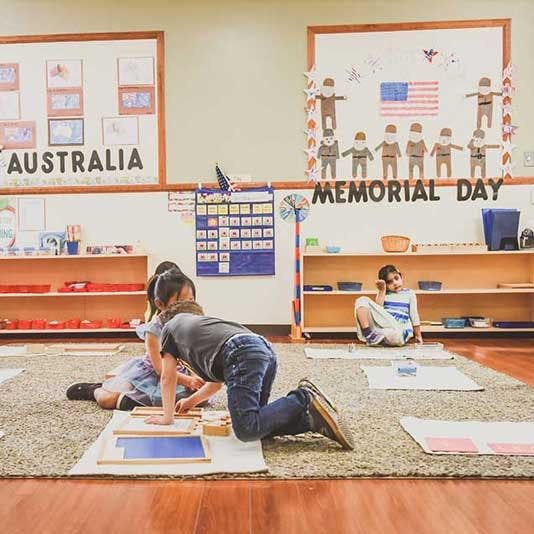 Children on a rug in a classroom, one kneeling and one sitting