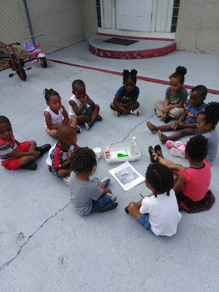 Group of children sitting in a circle on the ground, looking at items in-progress activity