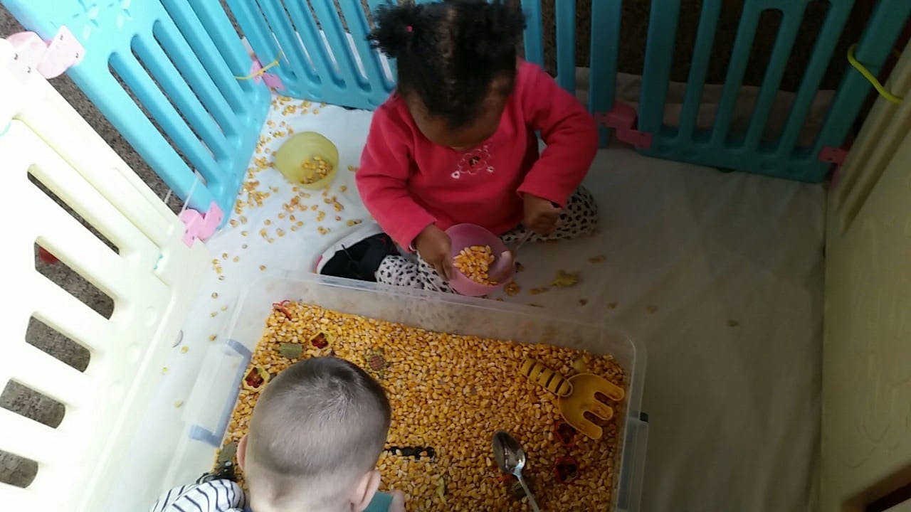 Child playing with corn kernels in a playpen