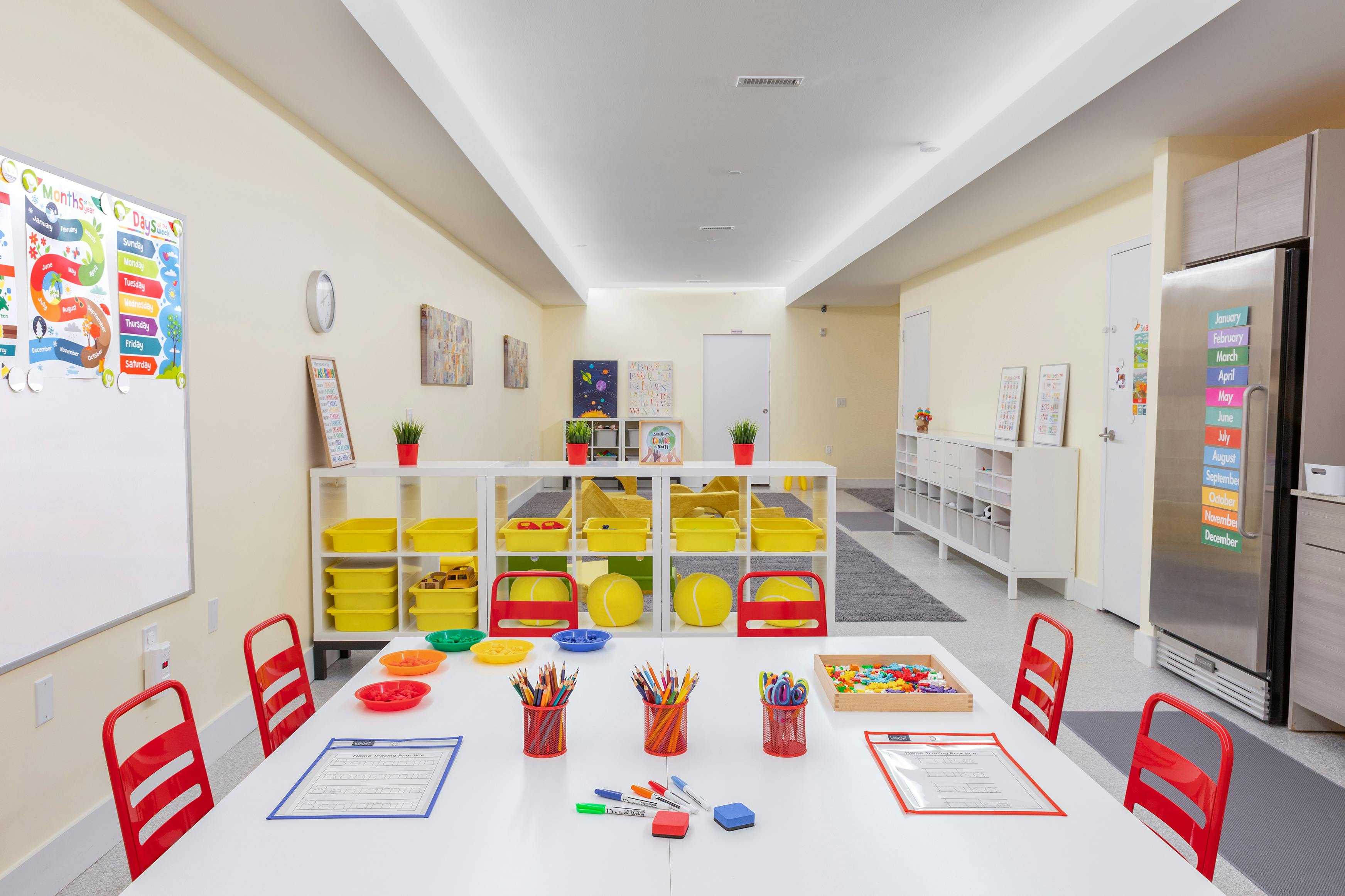 A colorful classroom with art supplies on a white table and various learning aids