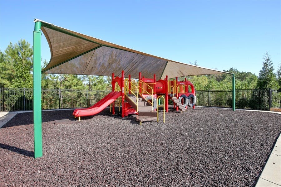 Playground with red slides and climbing structures under a shade sail