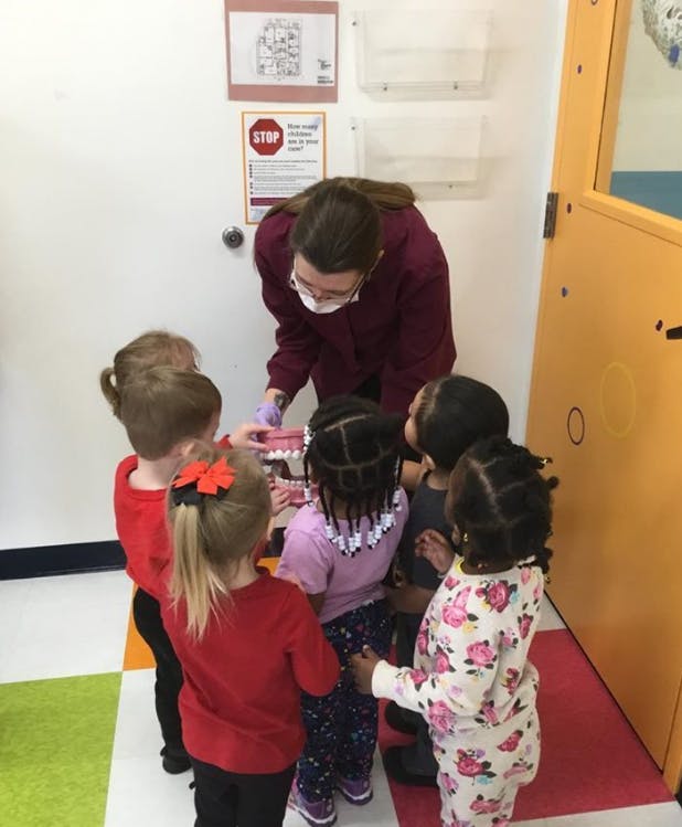 Person in mask and gloves demonstrating dental hygiene to children