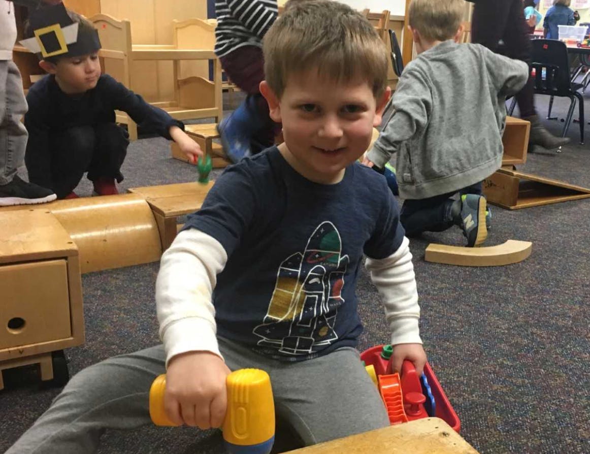Child holding a toy hammer in a classroom
