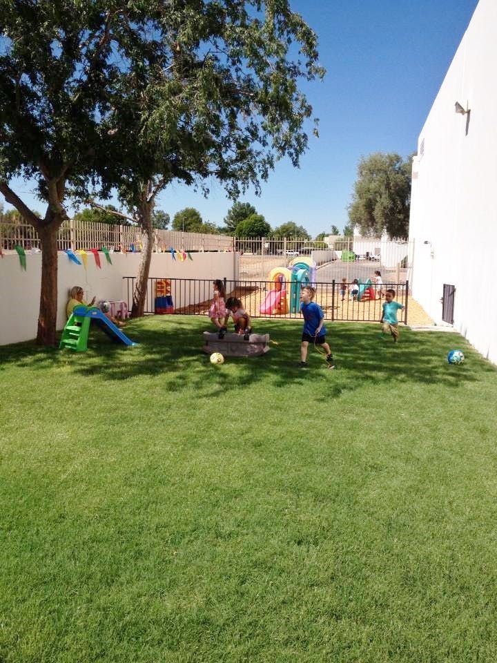 Children playing on a grassy playground with a slide and toys