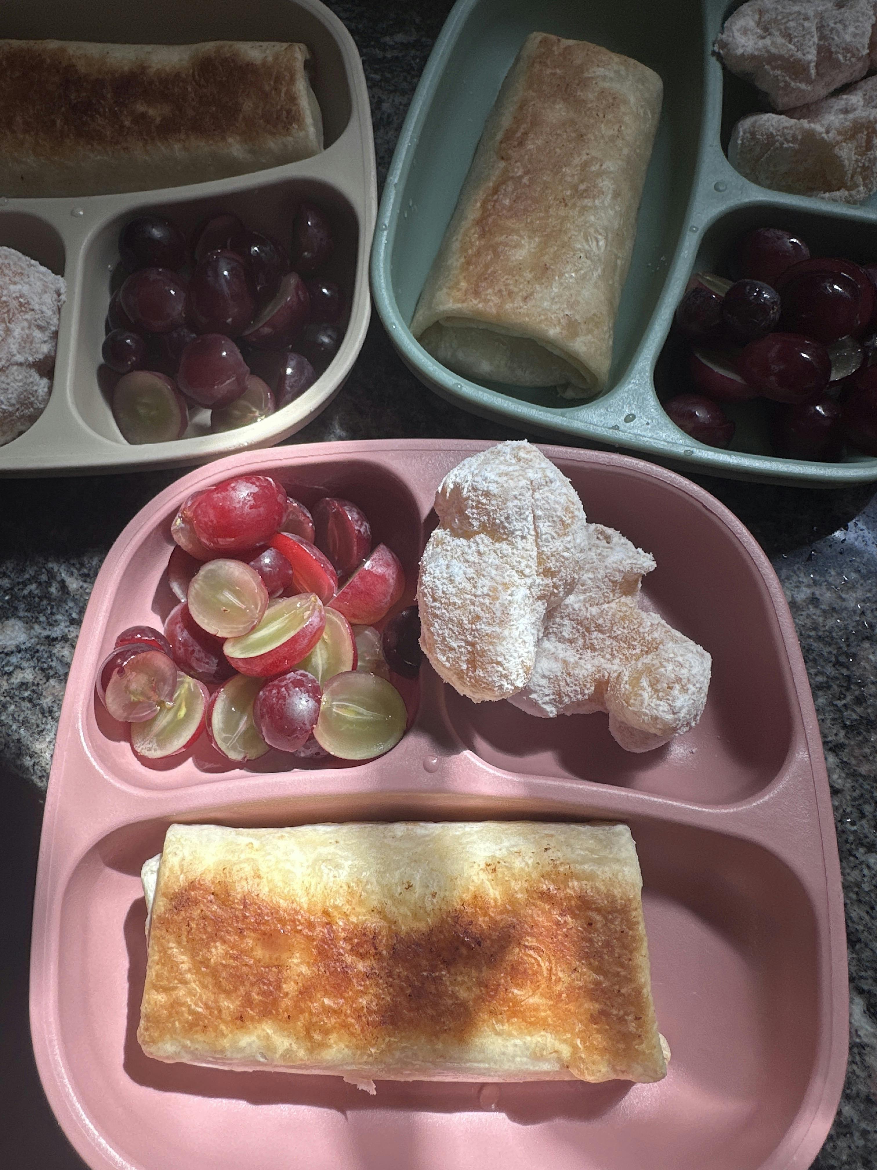 Several divided plates with burritos, grapes, and powdered sugar pastries