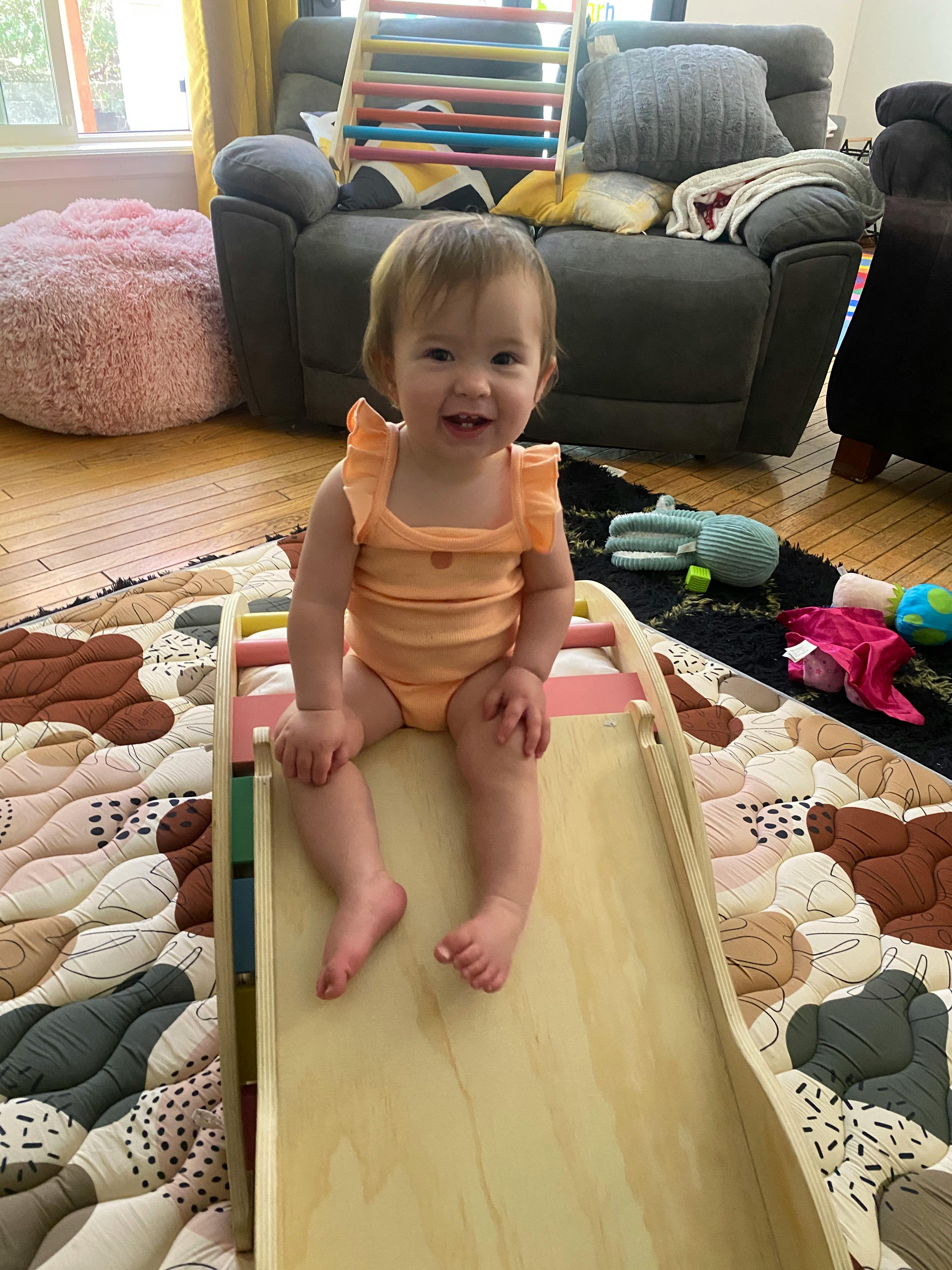 Smiling child sitting on a wooden indoor slide with legs outstretched