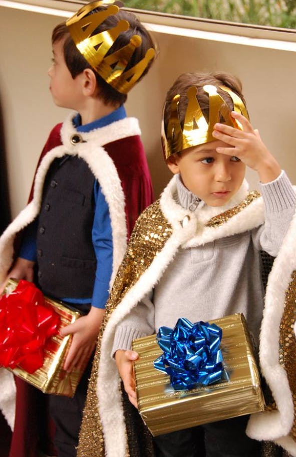 Two children wearing crowns and capes, holding wrapped gifts