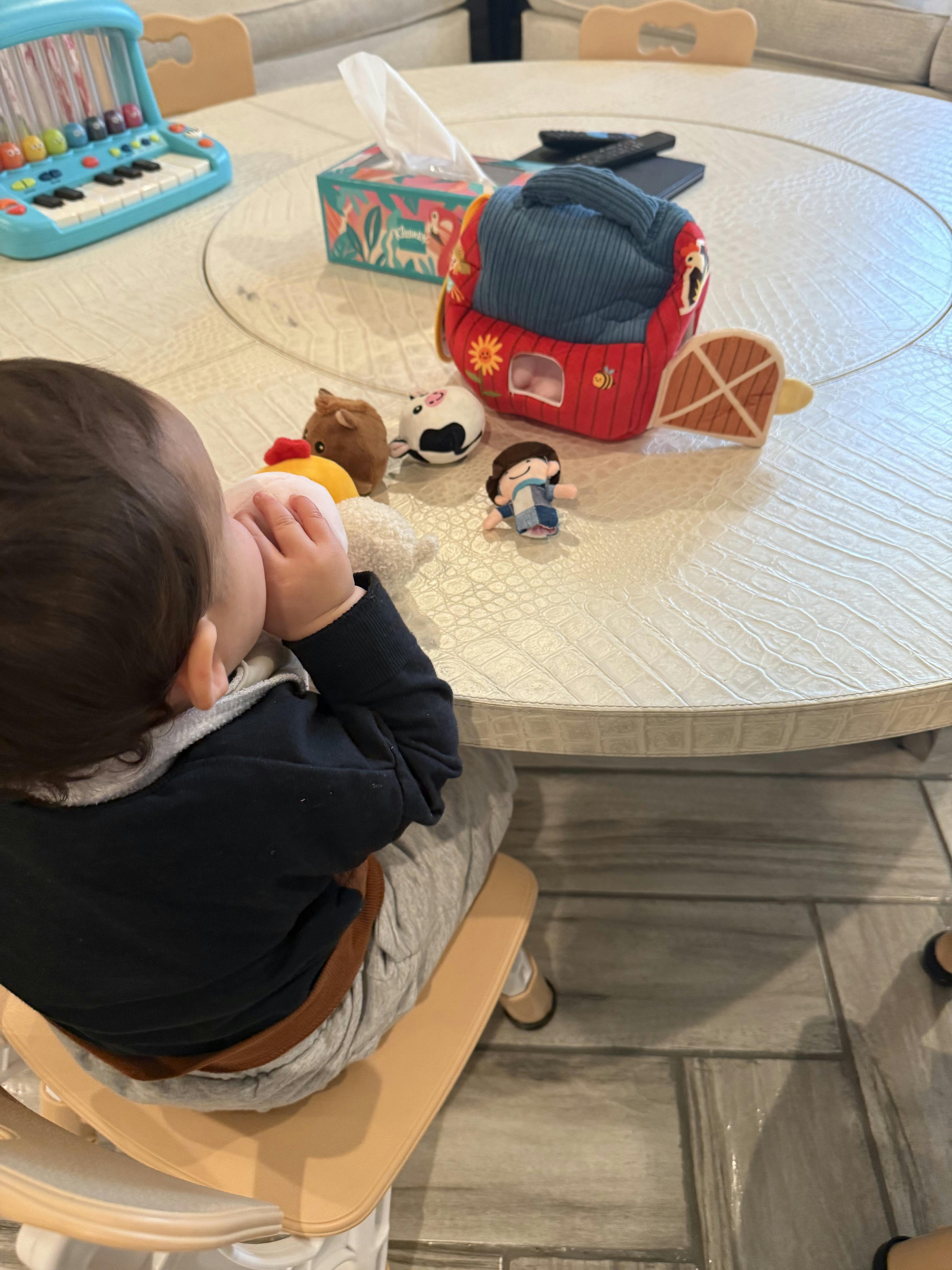 Child in a high chair playing with farm animal toys on a table