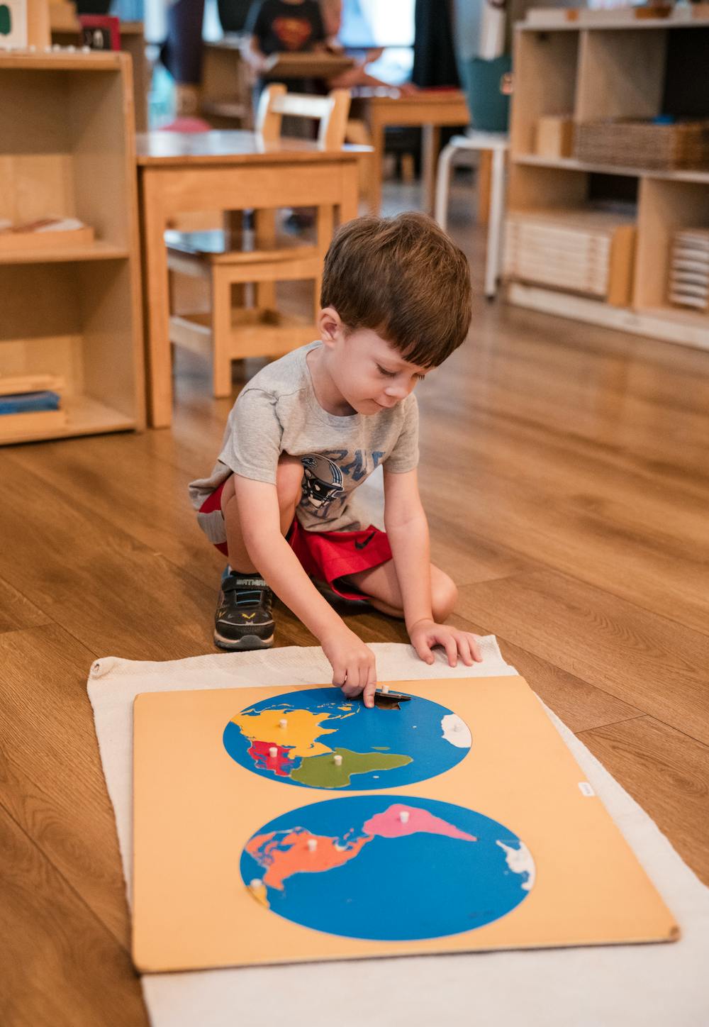 Child assembling a world map puzzle on the floor in a classroom
