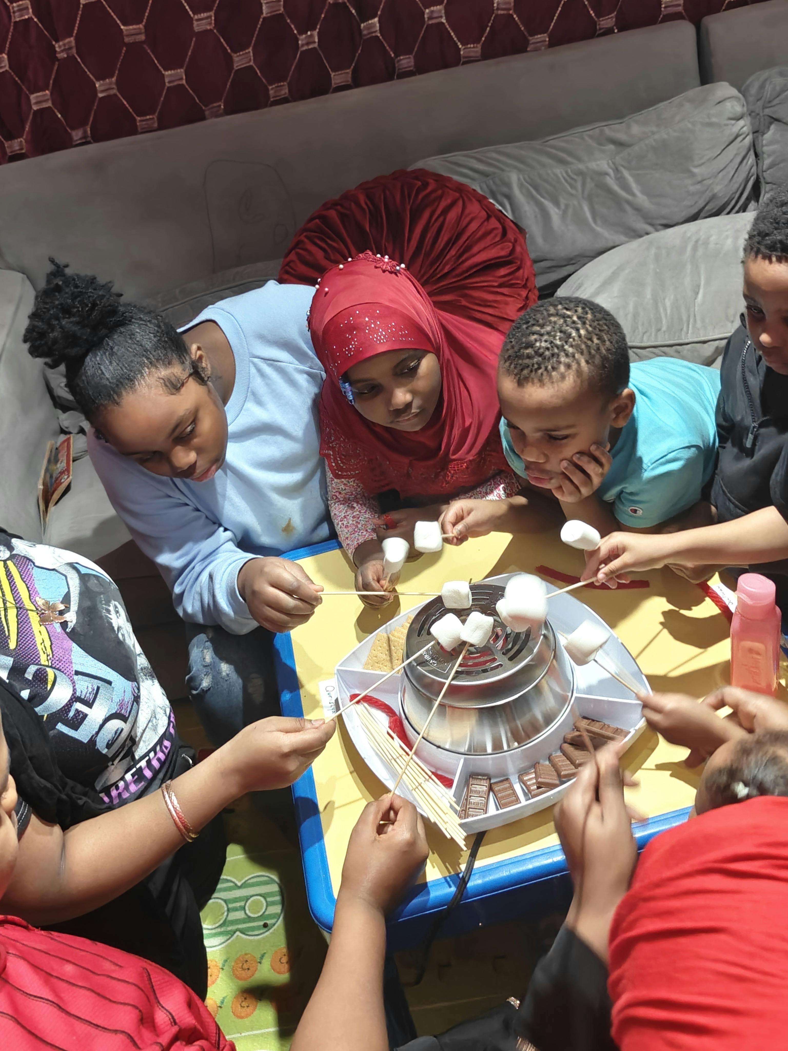 Children gathered around a fondue set with marshmallows on sticks