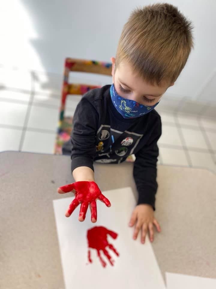 Child with red paint on hand making a handprint on paper