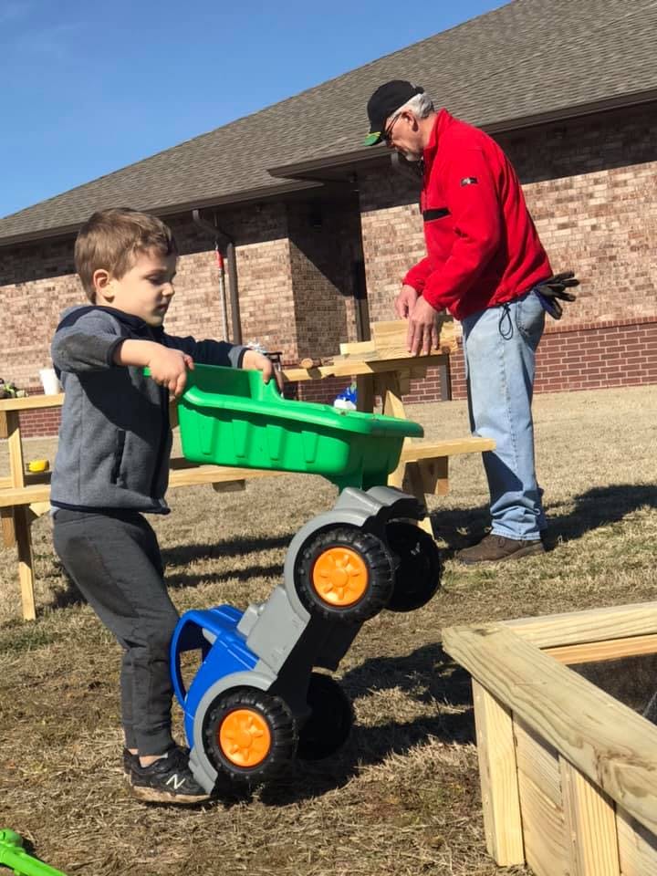 Child playing with a toy truck while an adult stands nearby