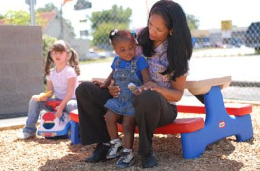 Person sitting with a child on a small picnic table, another child nearby