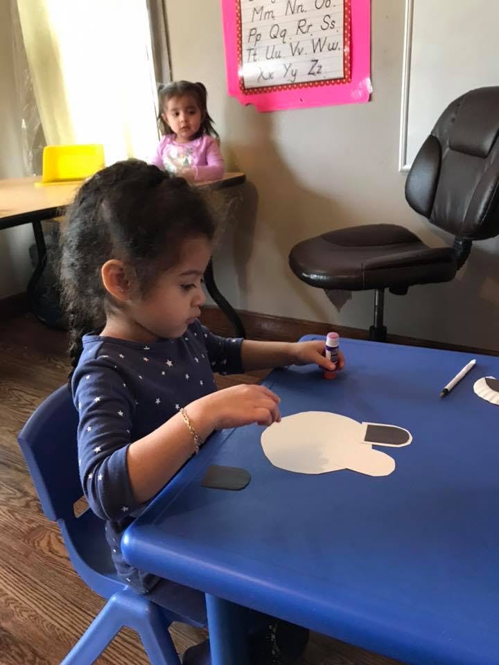 Child at a blue table doing a craft with paper cutouts and glue